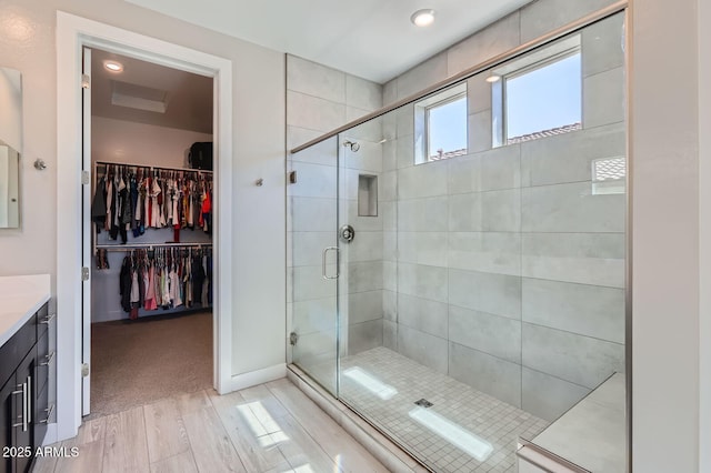 bathroom featuring baseboards, a spacious closet, a stall shower, and vanity