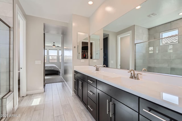 ensuite bathroom featuring double vanity, baseboards, a stall shower, and a sink