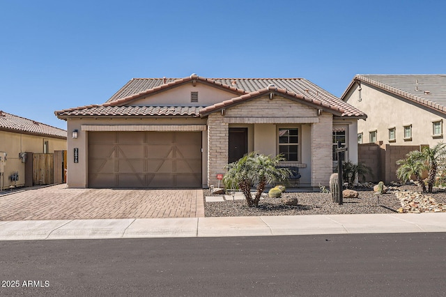 view of front of house with a tiled roof, decorative driveway, an attached garage, and fence