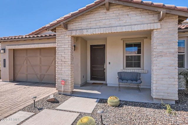 view of front facade featuring stucco siding, a tile roof, decorative driveway, a porch, and an attached garage