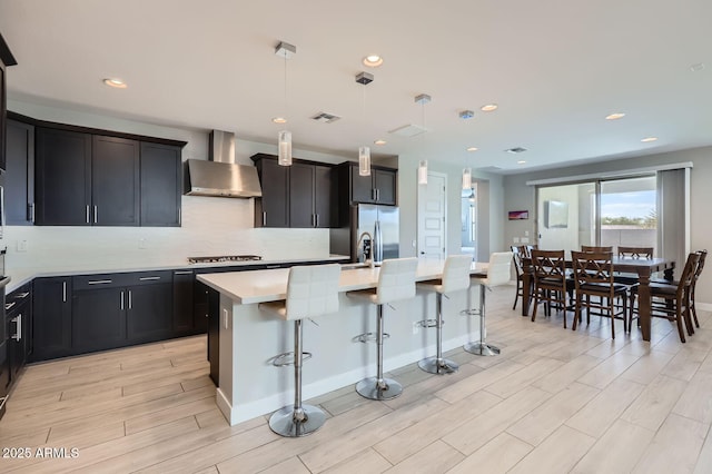 kitchen featuring visible vents, wall chimney range hood, a breakfast bar area, light countertops, and a kitchen island with sink