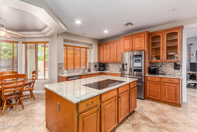 kitchen with a raised ceiling, stainless steel appliances, backsplash, a center island, and ceiling fan