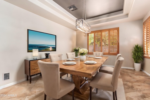 tiled dining space with a raised ceiling and a chandelier