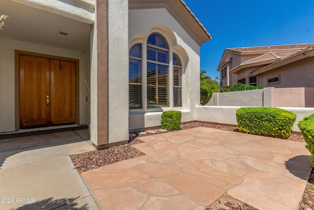 property entrance with stucco siding, a patio, and fence