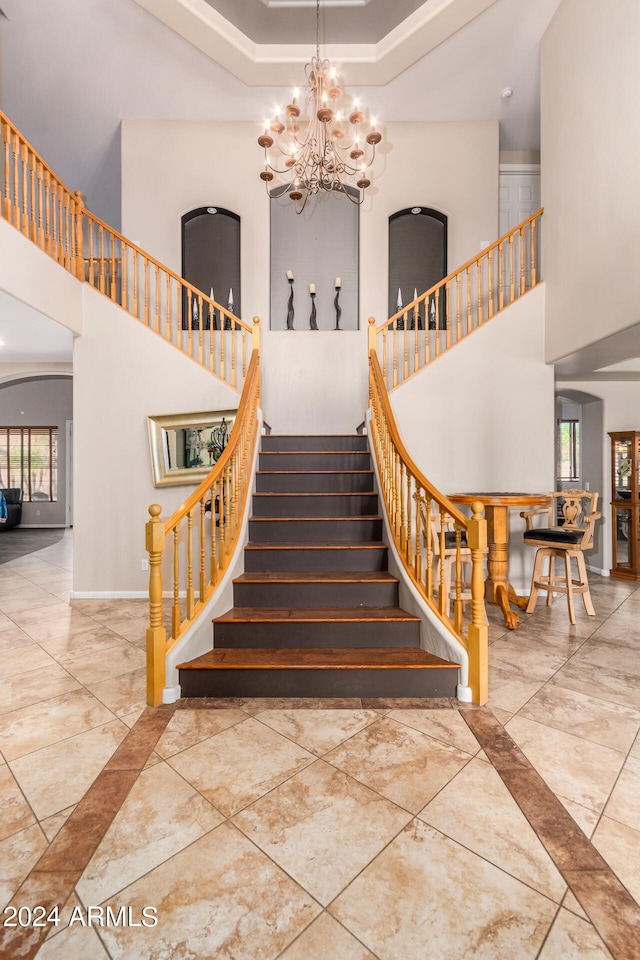 staircase featuring tile patterned floors, a wealth of natural light, a chandelier, and a towering ceiling