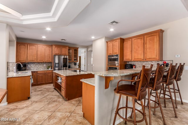 kitchen featuring light stone countertops, a peninsula, a sink, appliances with stainless steel finishes, and brown cabinets