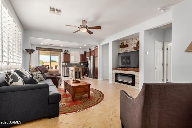 living area with light tile patterned flooring, a fireplace, visible vents, and a ceiling fan