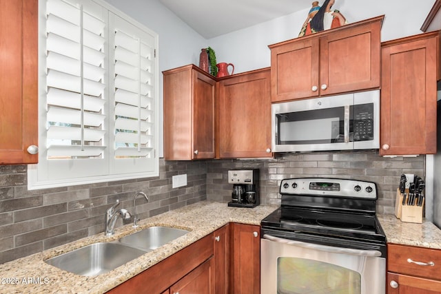 kitchen featuring stainless steel appliances, backsplash, brown cabinetry, a sink, and light stone countertops