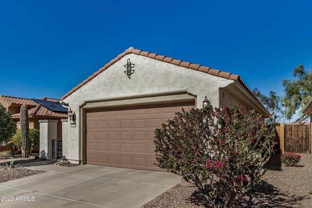 view of home's exterior featuring a garage, fence, concrete driveway, a tiled roof, and stucco siding