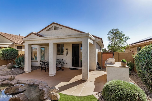 back of property featuring stucco siding, a tile roof, fence, and a patio