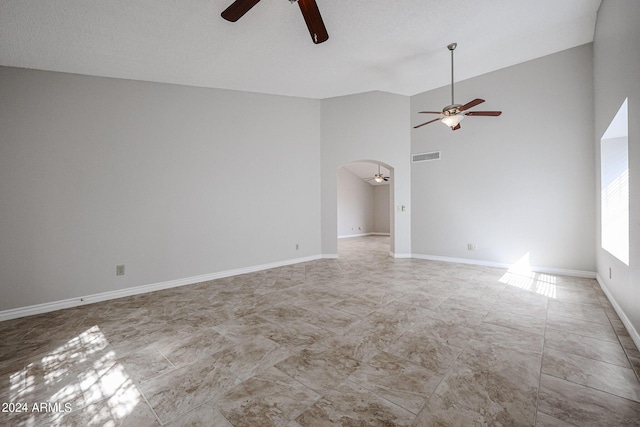 empty room featuring arched walkways, visible vents, a ceiling fan, high vaulted ceiling, and baseboards