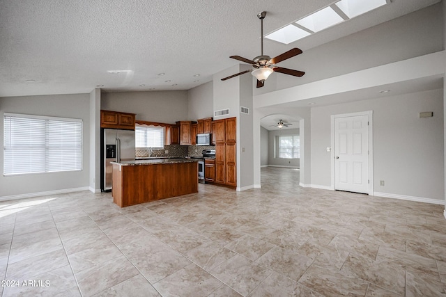 kitchen with stainless steel appliances, open floor plan, a kitchen island, ceiling fan, and plenty of natural light