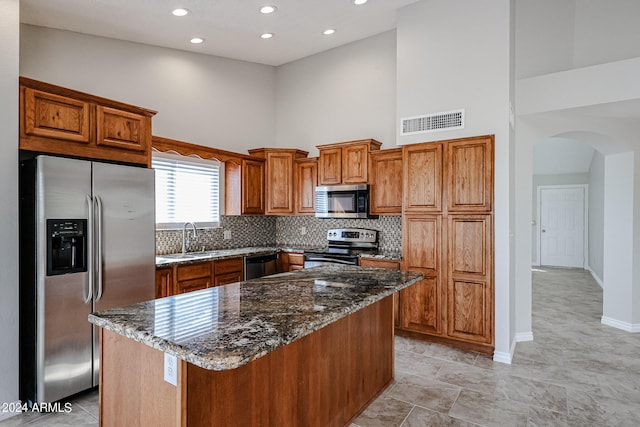 kitchen featuring arched walkways, stainless steel appliances, visible vents, a towering ceiling, and a sink