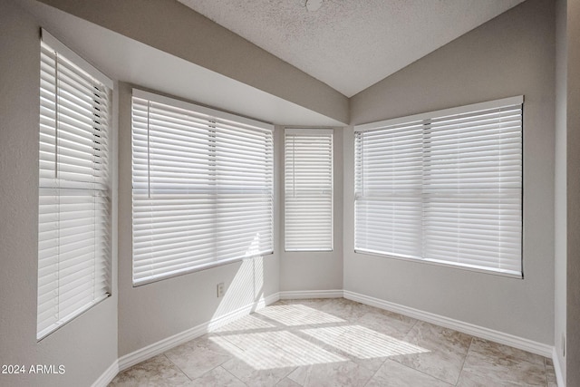 unfurnished room with vaulted ceiling, a textured ceiling, and baseboards