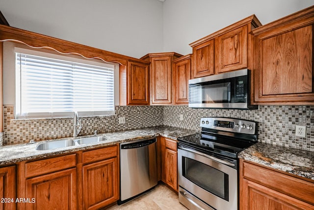 kitchen with a sink, appliances with stainless steel finishes, backsplash, brown cabinets, and dark stone counters