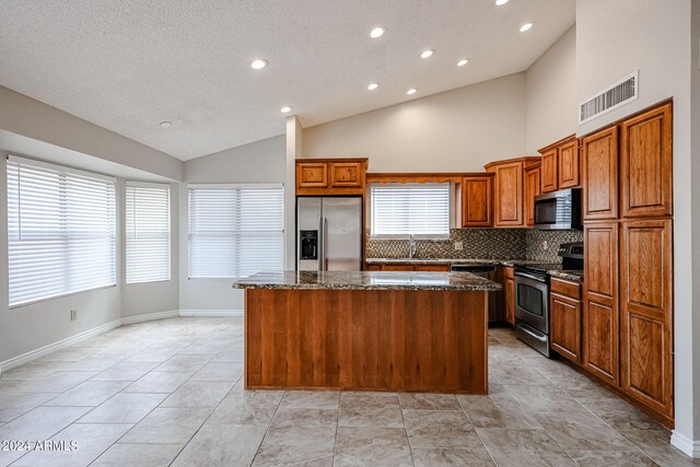 kitchen featuring visible vents, brown cabinetry, dark stone counters, a kitchen island, and appliances with stainless steel finishes