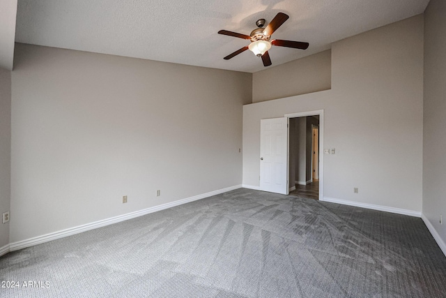 empty room with dark colored carpet, vaulted ceiling, ceiling fan, a textured ceiling, and baseboards