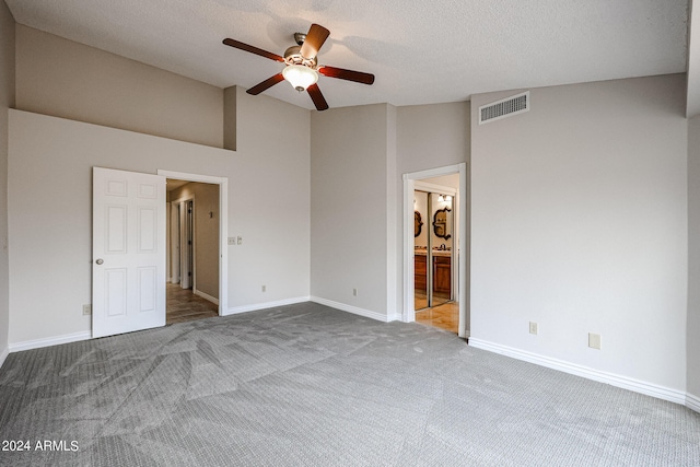 unfurnished bedroom with light carpet, high vaulted ceiling, a textured ceiling, connected bathroom, and ceiling fan