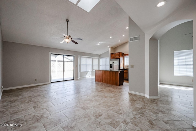 unfurnished living room with a ceiling fan, arched walkways, visible vents, and plenty of natural light