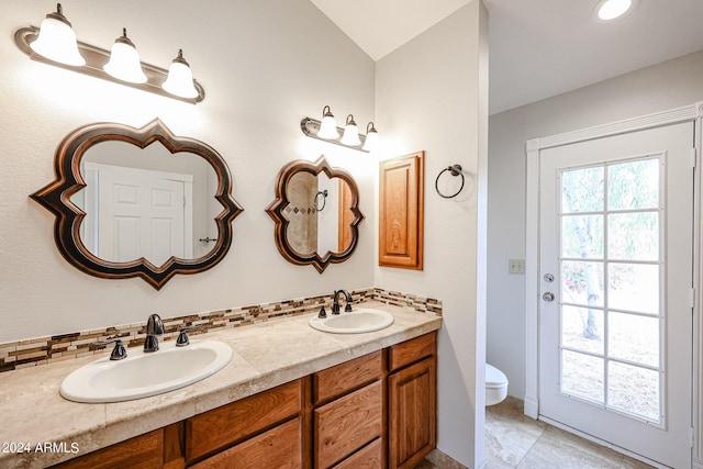 full bath featuring double vanity, tasteful backsplash, a sink, and toilet