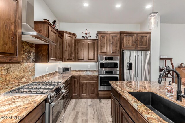 22050 W El Grande Trl, Wickenburg, AZ 85390 - kitchen with light wood-type flooring, light stone counters, wall chimney range hood, appliances with stainless steel finishes, and a sink