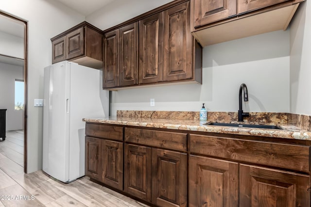 22050 W El Grande Trl, Wickenburg, AZ 85390 - kitchen with light wood-style floors, freestanding refrigerator, light stone countertops, dark brown cabinetry, and a sink