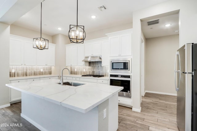 kitchen featuring light stone countertops, stainless steel appliances, sink, pendant lighting, and an island with sink