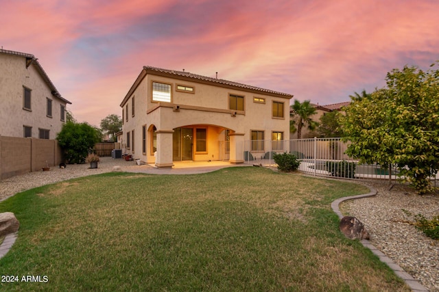 back house at dusk featuring a yard and a patio