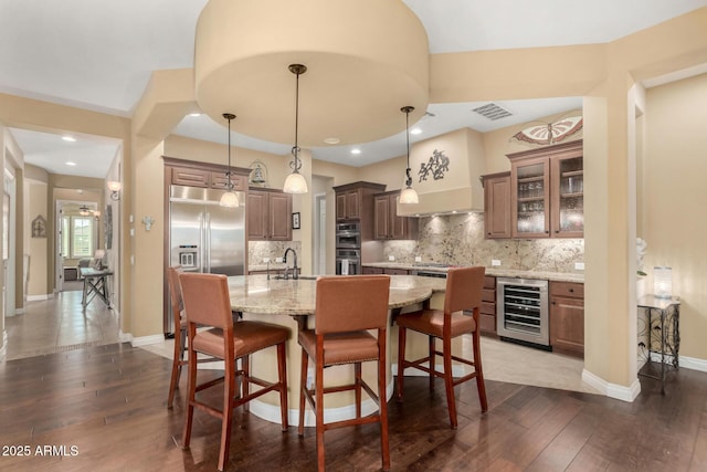 kitchen featuring a kitchen island with sink, hanging light fixtures, dark hardwood / wood-style floors, and beverage cooler