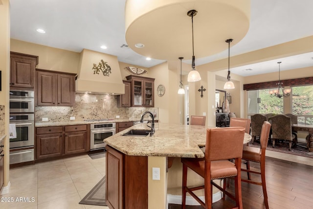 kitchen with premium range hood, sink, backsplash, stainless steel appliances, and light stone countertops