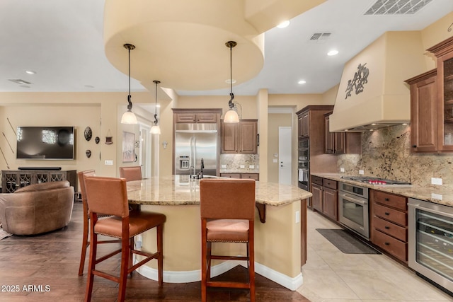 kitchen featuring stainless steel appliances, a center island with sink, wine cooler, and a kitchen bar