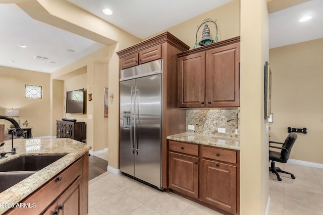 kitchen featuring stainless steel built in refrigerator, sink, decorative backsplash, light tile patterned floors, and light stone counters