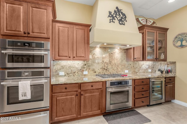 kitchen with custom exhaust hood, light stone counters, tasteful backsplash, appliances with stainless steel finishes, and beverage cooler