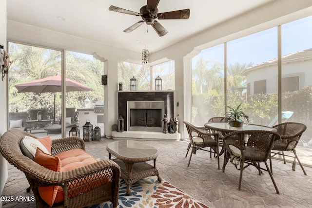 sunroom with an outdoor fireplace, plenty of natural light, and ceiling fan