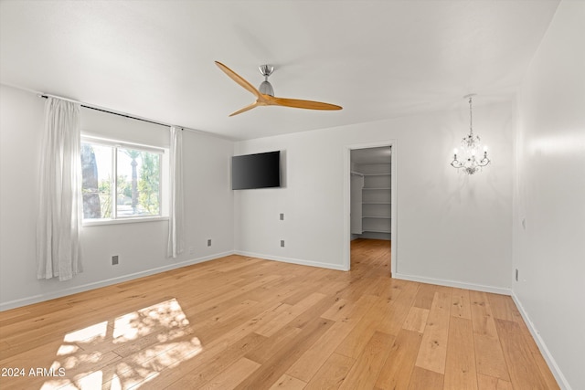 empty room featuring ceiling fan with notable chandelier and light hardwood / wood-style flooring