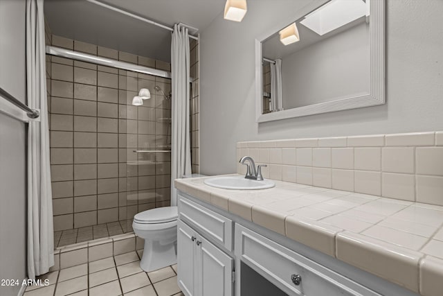 bathroom featuring a skylight, tile patterned floors, vanity, tiled shower, and toilet