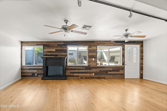 unfurnished living room featuring ceiling fan, wood walls, and light wood-type flooring