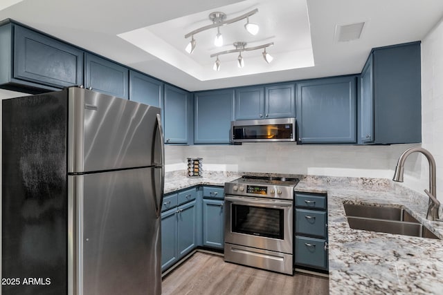 1075 E Chandler Blvd Unit 210, Chandler, AZ 85225 - kitchen featuring appliances with stainless steel finishes, blue cabinetry, a tray ceiling, light wood-style floors, and light stone countertops