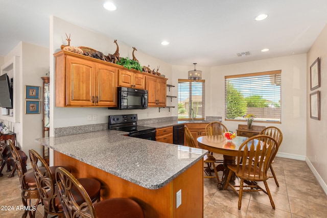 kitchen featuring kitchen peninsula, hanging light fixtures, light stone countertops, black appliances, and sink