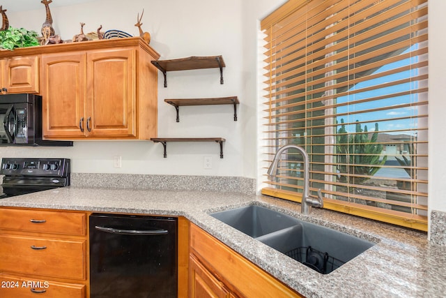 kitchen with light stone counters, black appliances, and sink