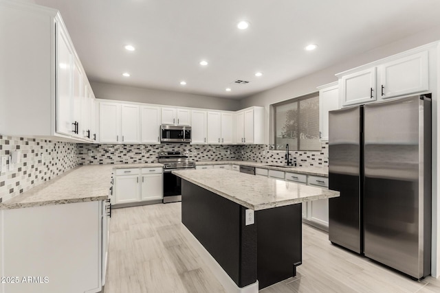 kitchen featuring sink, white cabinetry, light stone counters, a kitchen island, and stainless steel appliances