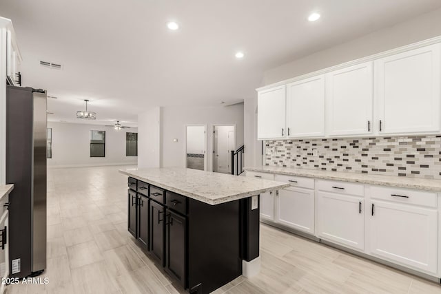 kitchen featuring stainless steel refrigerator, tasteful backsplash, white cabinetry, a center island, and light stone counters
