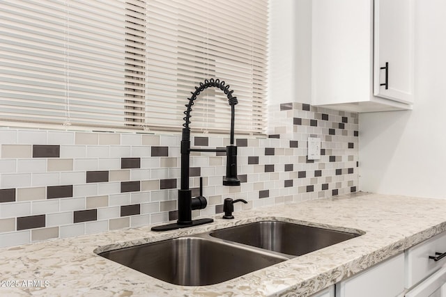 interior details featuring white cabinetry, sink, light stone counters, and tasteful backsplash