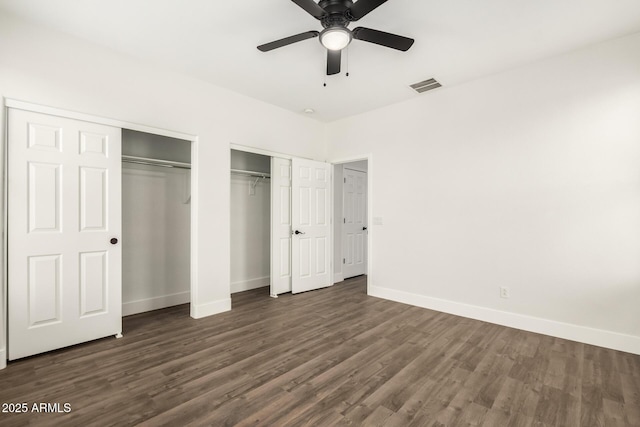 unfurnished bedroom with dark hardwood / wood-style flooring, ceiling fan, and multiple closets