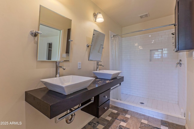 full bathroom featuring visible vents, a sink, double vanity, and tiled shower