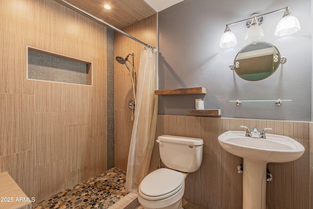 bathroom with wainscoting, toilet, and tiled shower