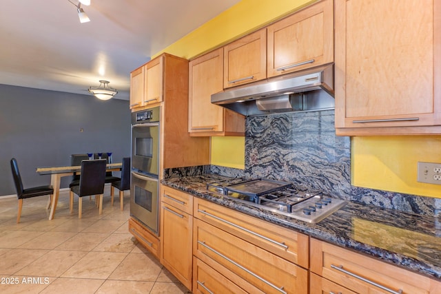 kitchen with light tile patterned floors, under cabinet range hood, dark stone countertops, appliances with stainless steel finishes, and backsplash