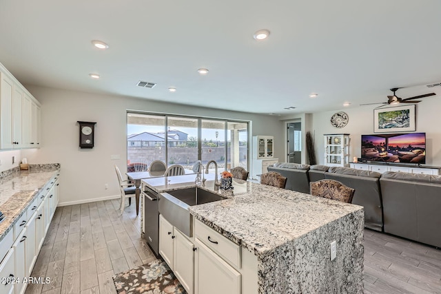 kitchen with sink, light wood-type flooring, a center island with sink, and white cabinets