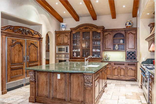 kitchen featuring a kitchen island with sink, sink, beam ceiling, and stainless steel appliances