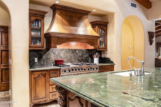 kitchen with sink, stone counters, range, tasteful backsplash, and custom range hood